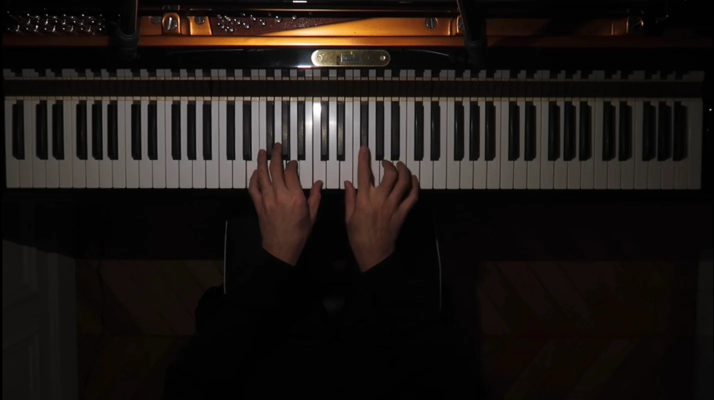 Both hands playing on a grand piano keyboard, lit from above.